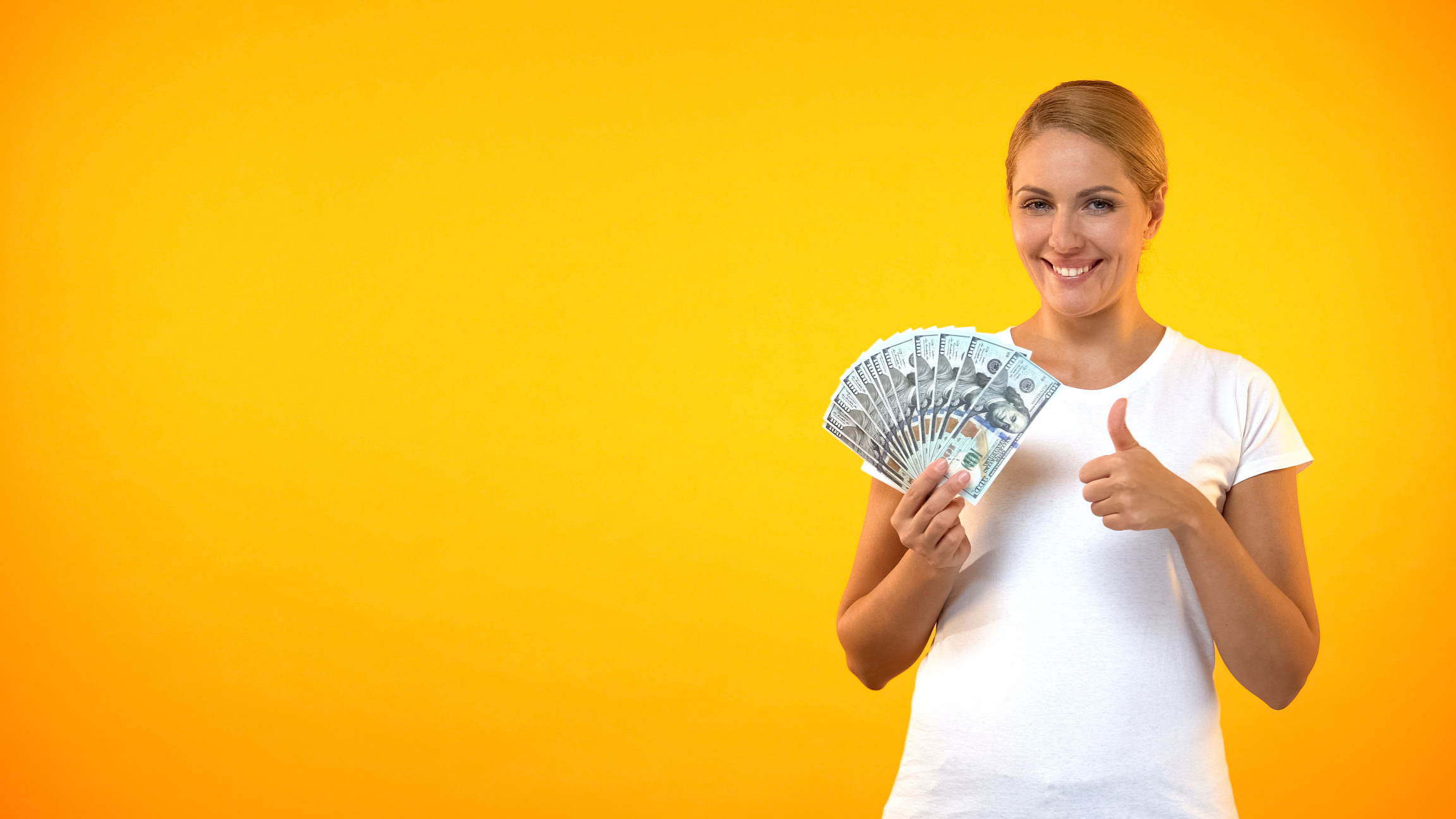 Pretty smiling woman showing thumbs up holding dollars, cashback service, credit